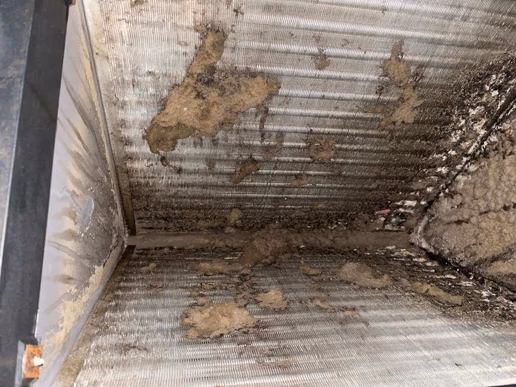 Close-up of an HVAC coil with accumulated dust and dirt buildup on the metal fins.