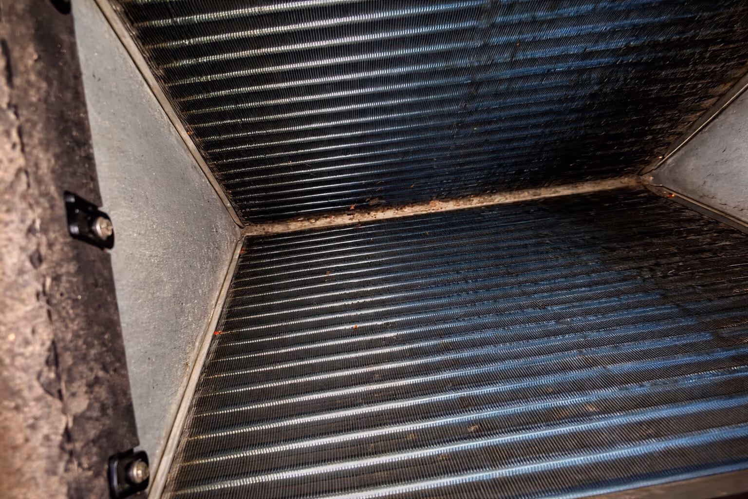 Close-up of a metallic, ribbed surface inside a rectangular space with some dirt and rust along the edges.