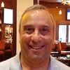 Smiling middle-aged man with short gray hair in a restaurant setting.